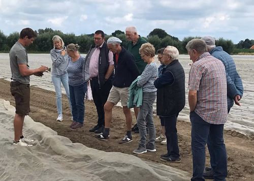 Gruppe von Personen, darunter Vertreter:innen der USD, SPD und Grünen, im Gespräch mit dem Landwirt des Biohofs Groß Wege in Lankern auf einem Feld – Themen: nachhaltige Landwirtschaft, Fruchtfolge und regionale Vermarktung.